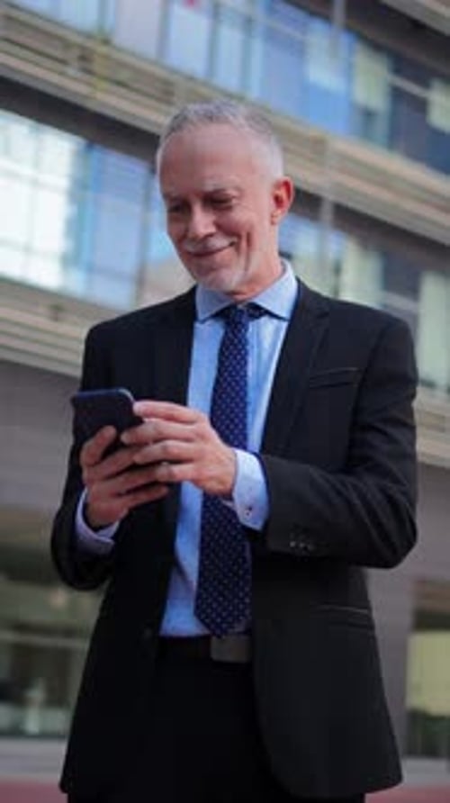 Vertical Middle Aged Businessman Using a Cellphone to Watch His Finances Outside Mature Business Man