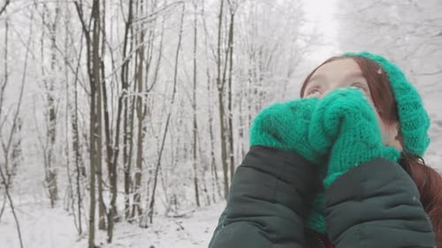 Woman in winter forest looking upward, enjoying snow