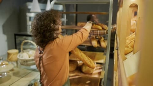 Female Sales Assistant Organizing Fresh Bread on Shelf in Bakery