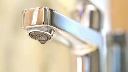 Shiny Silver Faucet with Dripping Water in a Bathroom
