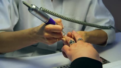 Manikürist schleift den Nagel einer Frau mit einem Nagelbohrer.
