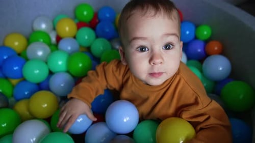 Toddler in orange shirt sitting in the soft basin among the bright balls.