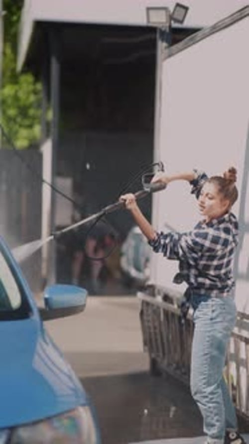 Woman Washing Car at Outdoor Carwash on Sunny Day
