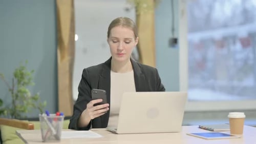 Woman at Desk Using Phone and Laptop