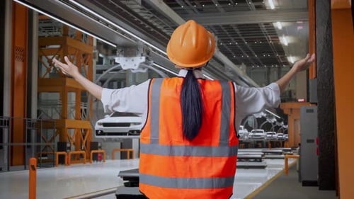 Une ingénieure étend les bras dans une usine de voitures électriques