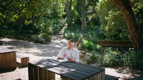 Woman Sitting Park Table Park with Smartphone Writing Information Into Notebook