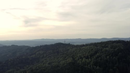 Weit aufragende Luftaufnahme von hügeligem Wald und ferner Stadt in Mitteleuropa