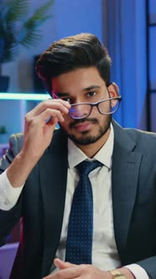 Smiling Young Man in Suit Takes Off Glasses Indoors
