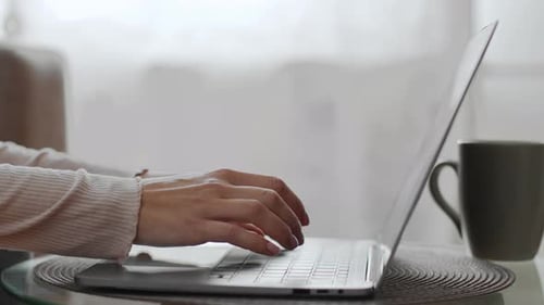 Woman Typing on Laptop Computer Next to Mug