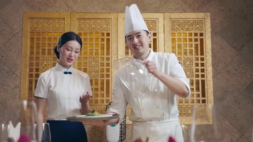 The hotel chef and waiter serve the dishes, holding a plate of food with a clear dome on top.