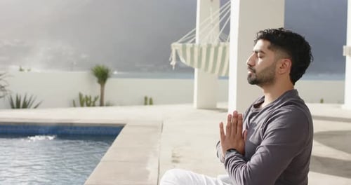 Indian man starting meditation by pressing palms together and breathing on pool terrace, copy space