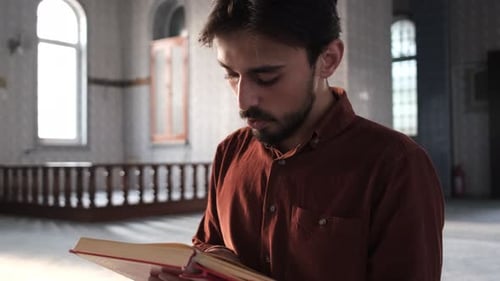 El hombre sentado en la mezquita leyendo el libro religioso del Corán mientras tarareaba, el musulmán sujetándolo