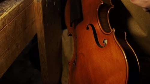 Italian violin maker applying varnish to a violin in a warmly lit workshop