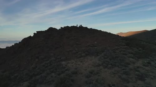 Three people standing on a cliff below the Pico de Teide mountain looking out on the hillside and a