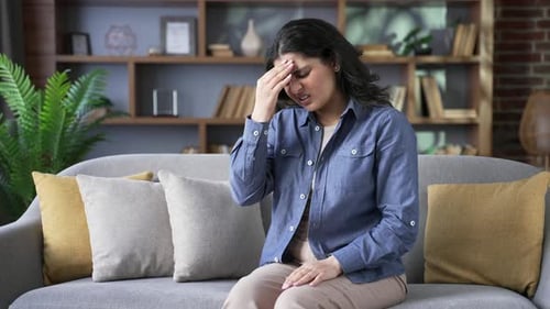 Woman with Headache Massaging Temple on a Sofa