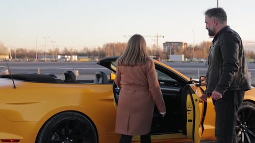Couple By Yellow Convertible Car at Sunset A Man Helps a Woman Get Into a Convertible Car