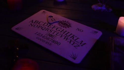 Close Up Video of a Wooden Ouija Board on a Table Surrounded By Candles Candlesticks and Other