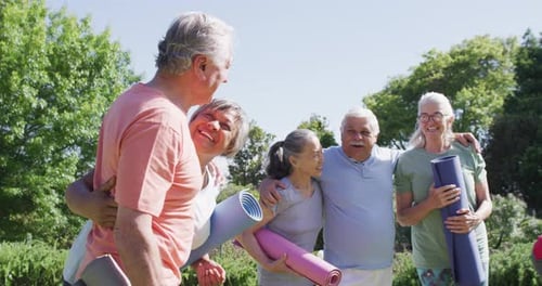 Diverse group of happy male and female seniors talking after exercising in sunny garden, slow motion