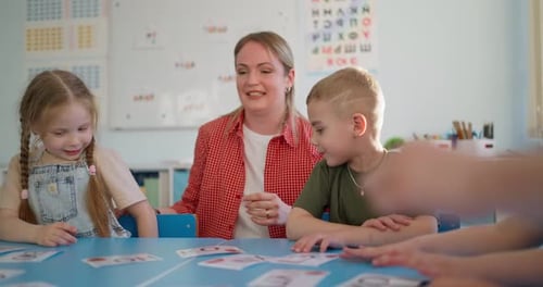 Young Children and Teacher Practice Letters with Flashcards at a Classroom Table During a Bright