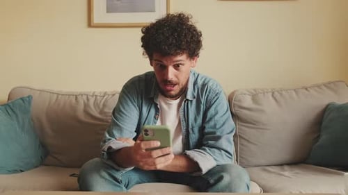 Young Man Using Smartphone Relaxing on Couch Indoors