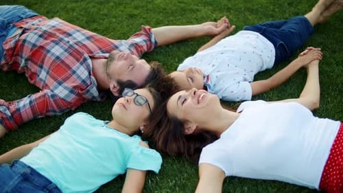 Closeup Smiling Family Lying In Circle On Green Grass Outdoors. Overhead View Positive Parents An...