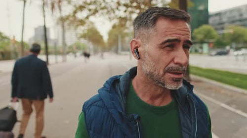 Close up, middle-aged man talking on headset, wireless earphone when walking in the square
