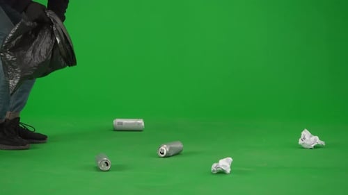 A Male Volunteer Wearing Black Gloves and Carrying a Trash Bag Picks Up Trash on the Green Screen
