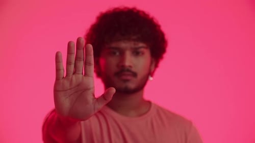 A Serious Stylish Indian Young Man Wears an Earring Shows Outstretched Hand and Open Palm The Stop