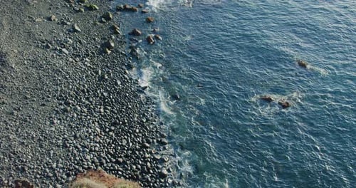Ocean Waves Crashing on volcanic streamlined stones at sunset. Black rocky beach, calm ocean, waves