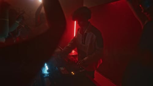 DJ Playing Electronic Music to Dancing Crowd in Red Neon Lit Nightclub