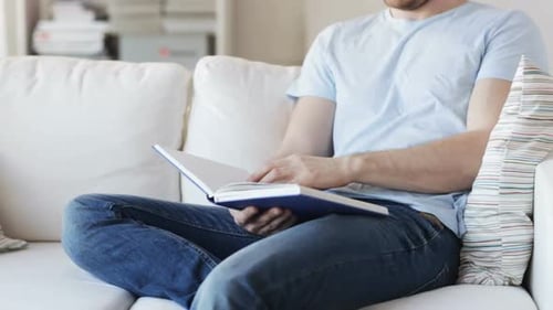 Man enjoying leisure time reading a novel on the couch at home learning