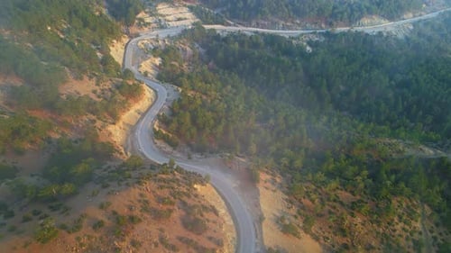 Aerial view of a winding foggy mountain road with trees in the background