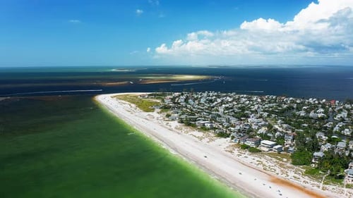 Coastal peninsula with beachfront community beside emerald waters and offshore sandbars — aerial vie