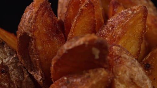Deep fried potato wedges or french fries rotate on black background
