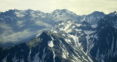 Majestic Mountain Range Showcases Snow Capped Peaks Under Cloudy Skies