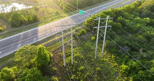 Linhas de energia em altos postes de aço se estendem por rodovias com carros de condução rápida e transmissão de eletricidade