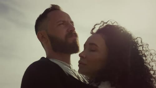 Multiethnic couple embracing on beach enjoying sunset sky wind in hair serenity