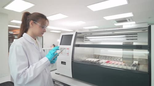 Woman lab technician operating machine for analysis