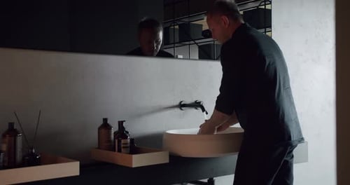 Man washing hands in domestic bathroom with loft interior