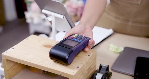 Closeup payment terminal placed on wooden counter inside flower shop ready to accept credit card