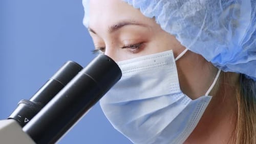 Woman Wearing Surgical Cap Looking Through Microscope