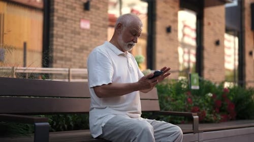 Senior Man Sits on Bench Using Mobile Phone