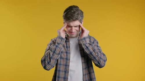 Man Rubbing Temples in Discomfort on Yellow Background