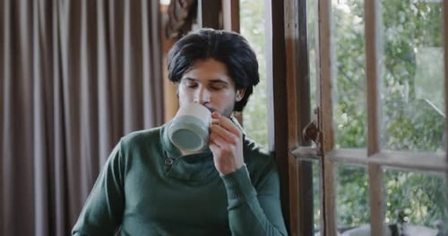 Man Drinks Coffee While Leaning Against a Window