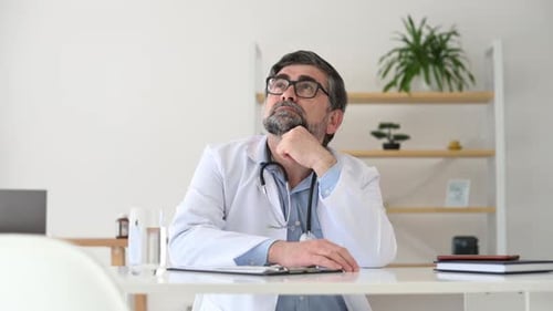 Mature male doctor in coat is in the clinic room