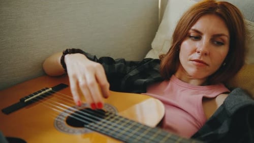 Woman plays acoustic guitar on couch at home