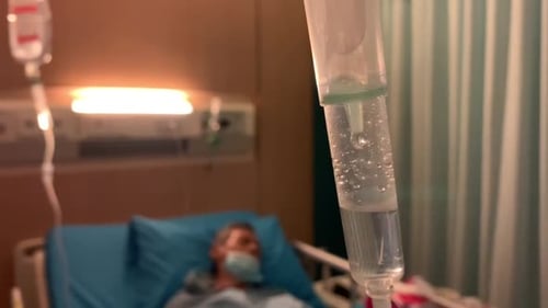 Intravenous drip treatment being used to treat a sick man lying on a bed in a hospital