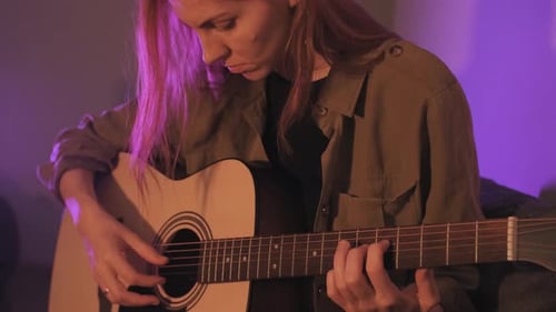 Young Woman Plays Acoustic Guitar Under Purple Lights