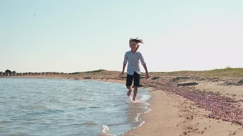 A Happy Teenager Runs Along the Ocean Shore Splashing Water with Bare Feet