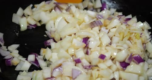 Onion pieces are fried in a pan.